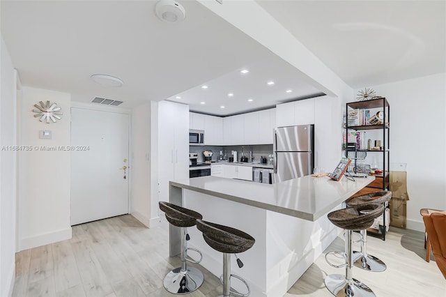 kitchen featuring white cabinetry, kitchen peninsula, appliances with stainless steel finishes, a kitchen bar, and light hardwood / wood-style flooring