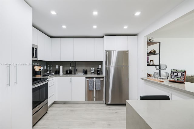 kitchen featuring stainless steel appliances, backsplash, sink, white cabinets, and light hardwood / wood-style flooring