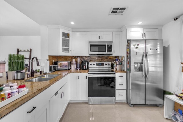 kitchen featuring stainless steel appliances, sink, tasteful backsplash, stone counters, and white cabinets