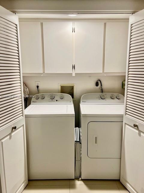 clothes washing area with washer and dryer, cabinets, and light tile patterned floors