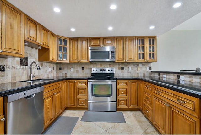 kitchen featuring stainless steel appliances, dark stone counters, decorative backsplash, sink, and light tile patterned floors