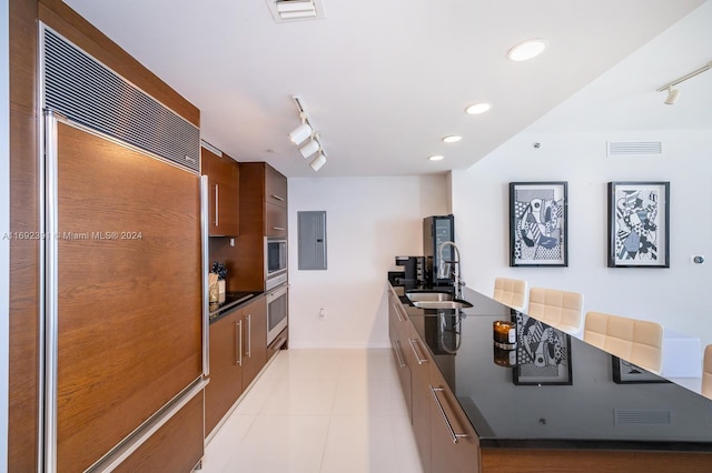 kitchen featuring rail lighting, paneled built in fridge, sink, and light tile patterned floors