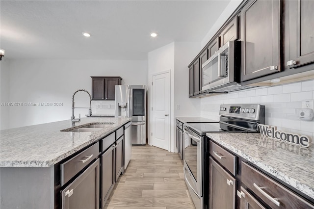 kitchen with stainless steel appliances, light stone countertops, sink, light hardwood / wood-style floors, and a kitchen island with sink