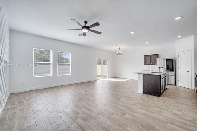 unfurnished living room with light wood-type flooring, ceiling fan with notable chandelier, and sink