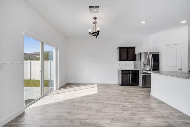 kitchen with dark brown cabinetry, light stone countertops, a chandelier, stainless steel fridge, and light wood-type flooring