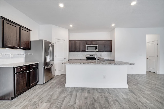 kitchen featuring tasteful backsplash, a kitchen island with sink, dark brown cabinets, light wood-type flooring, and appliances with stainless steel finishes