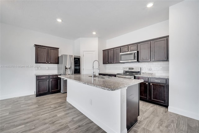 kitchen featuring stainless steel appliances, a center island with sink, sink, dark brown cabinets, and light wood-type flooring