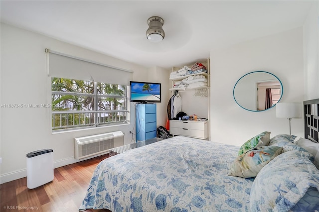 bedroom featuring ceiling fan, wood-type flooring, and an AC wall unit