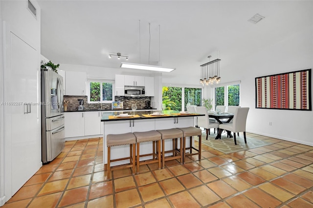 kitchen featuring appliances with stainless steel finishes, decorative light fixtures, white cabinetry, and a wealth of natural light