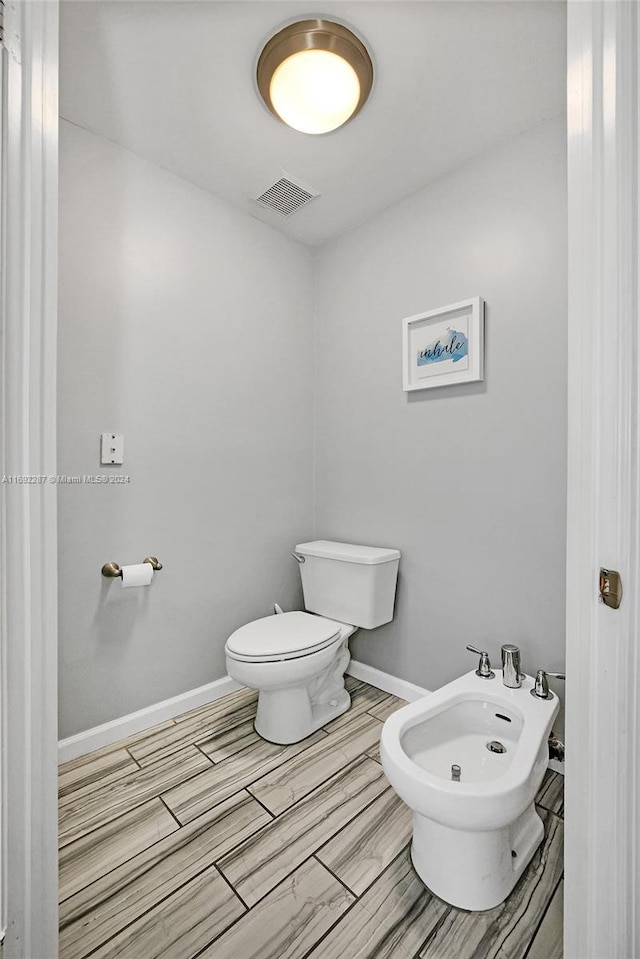 bathroom with toilet, wood-type flooring, and a bidet