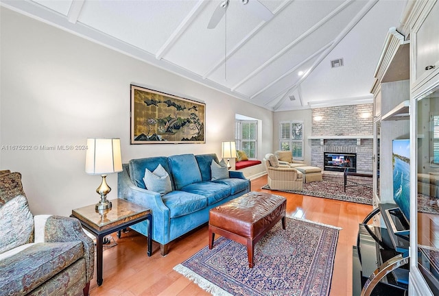 living room with ceiling fan, a brick fireplace, lofted ceiling with beams, a textured ceiling, and light wood-type flooring