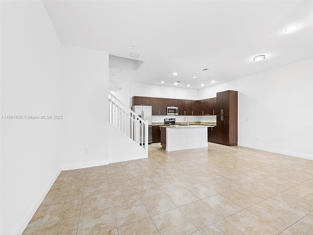 kitchen with appliances with stainless steel finishes, sink, light tile patterned floors, dark brown cabinets, and a center island with sink