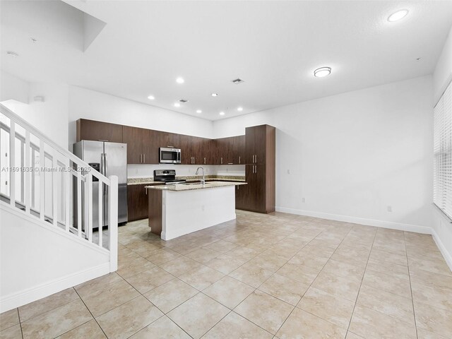 kitchen featuring sink, a center island with sink, stainless steel appliances, dark brown cabinetry, and light tile patterned flooring