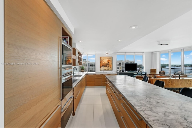 kitchen with a warming drawer, glass insert cabinets, light tile patterned flooring, stainless steel oven, and a sink