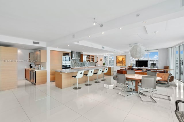 kitchen featuring modern cabinets, appliances with stainless steel finishes, a kitchen breakfast bar, wall chimney range hood, and backsplash