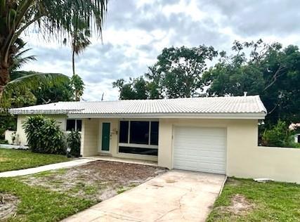 single story home featuring metal roof, an attached garage, concrete driveway, a front yard, and stucco siding