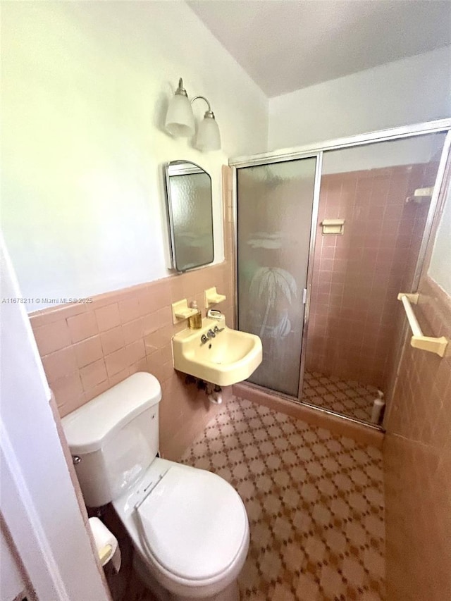 bathroom featuring a stall shower, a wainscoted wall, toilet, a sink, and tile walls