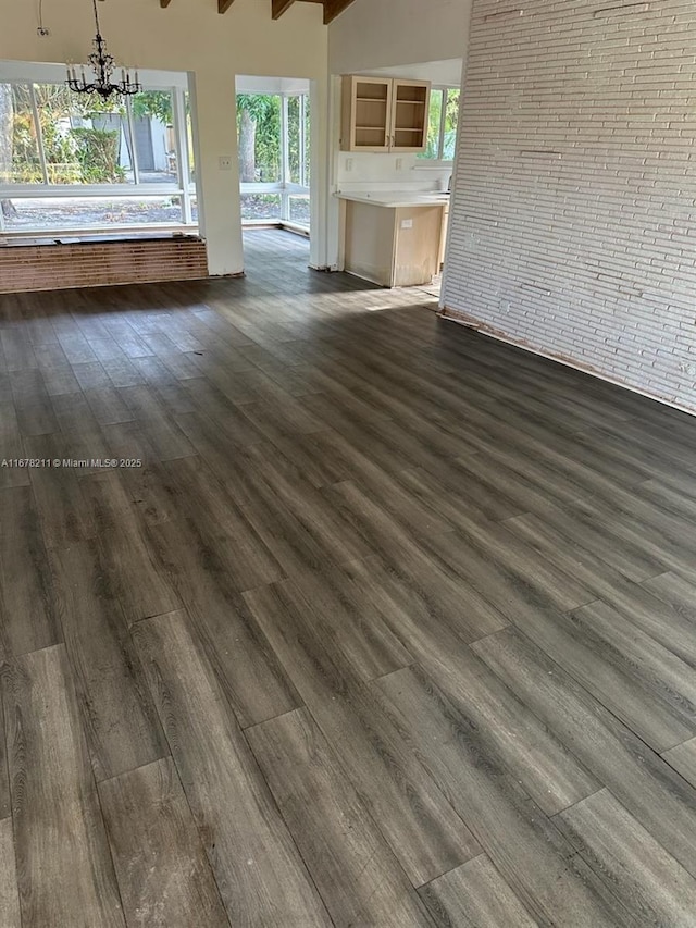 unfurnished living room with dark wood-style floors, brick wall, and a chandelier