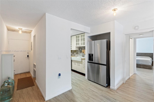 kitchen featuring a textured ceiling, white cabinetry, light wood-type flooring, and stainless steel refrigerator with ice dispenser