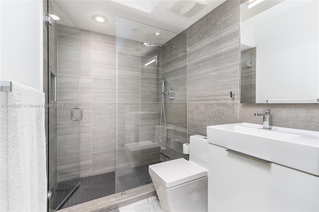 bathroom with tile walls, vanity, toilet, and a shower with shower door