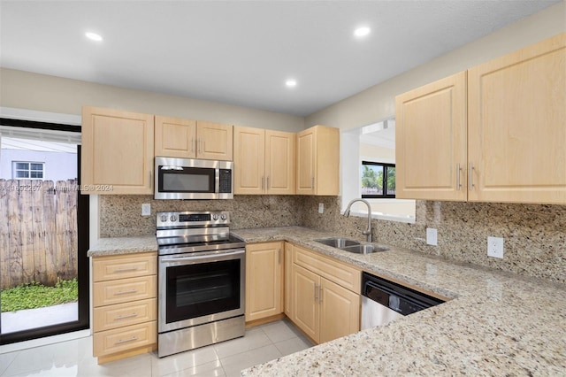 kitchen featuring light stone counters, appliances with stainless steel finishes, light tile patterned floors, light brown cabinetry, and sink