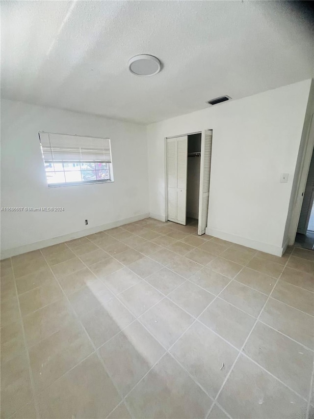 unfurnished bedroom featuring a textured ceiling, light tile patterned floors, and a closet