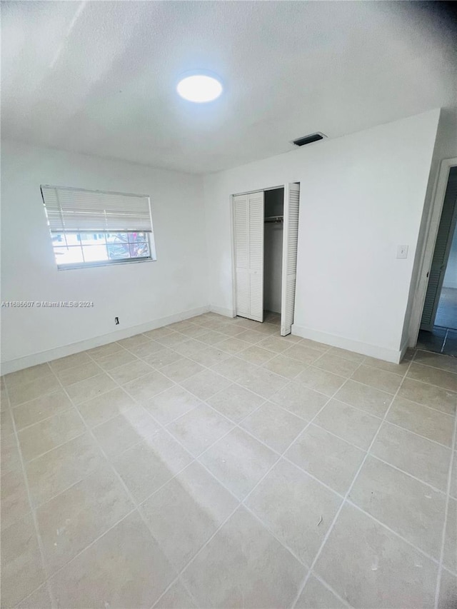 unfurnished bedroom with a textured ceiling, light tile patterned floors, and a closet