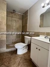 bathroom featuring tile patterned flooring, vanity, toilet, and tiled shower