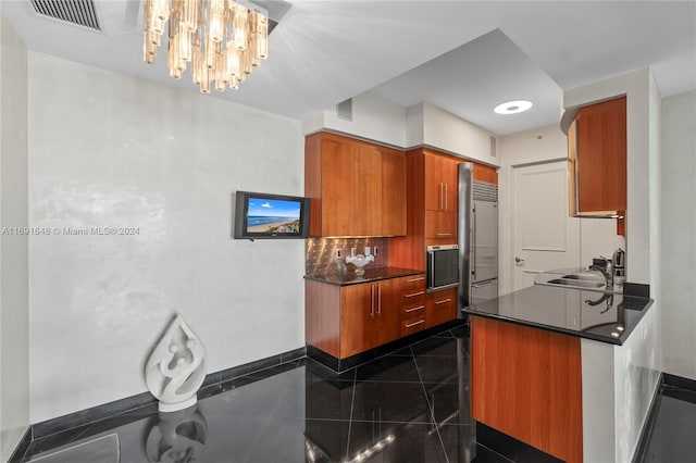 kitchen with an inviting chandelier, sink, dark tile patterned floors, kitchen peninsula, and stainless steel appliances