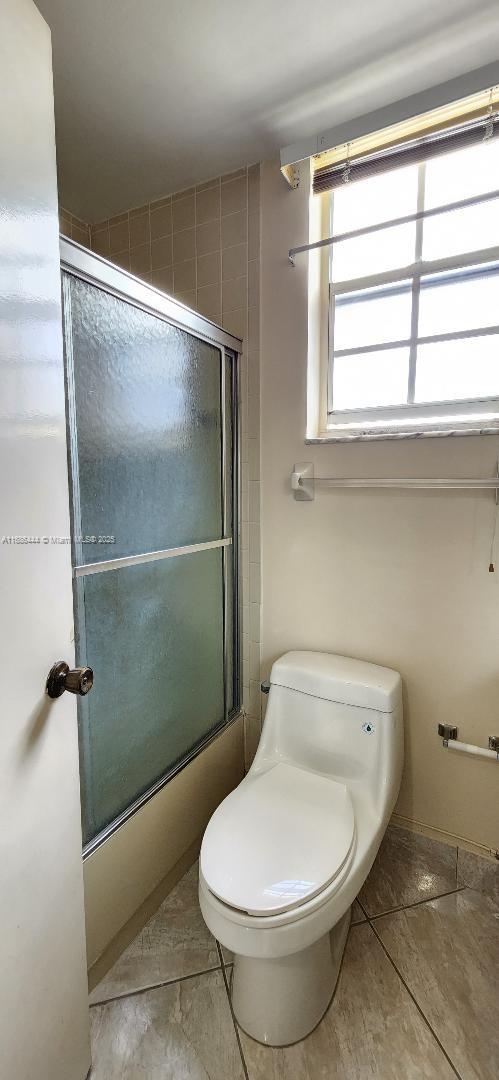 bathroom with bath / shower combo with glass door and toilet