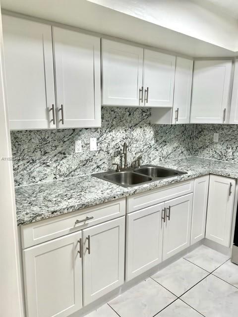 kitchen featuring decorative backsplash, sink, light stone counters, and white cabinets