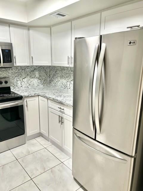 kitchen with white cabinets, decorative backsplash, light stone counters, and stainless steel appliances