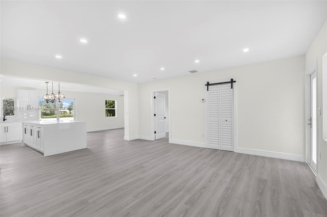 unfurnished living room featuring a chandelier, a barn door, and light hardwood / wood-style floors