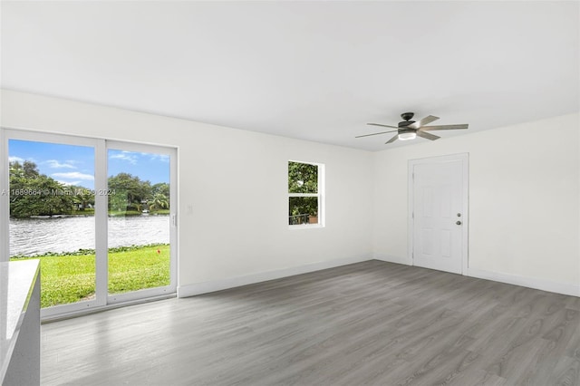 unfurnished room with a water view, wood-type flooring, and ceiling fan