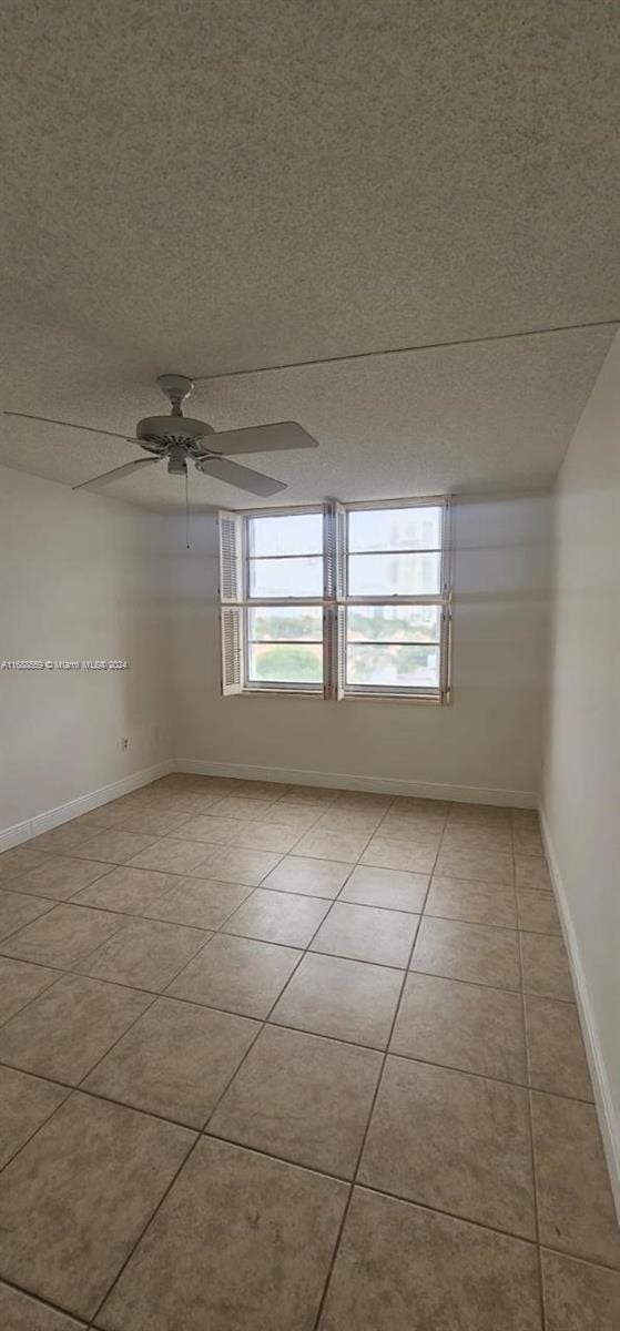 spare room with a textured ceiling, light tile patterned flooring, and ceiling fan