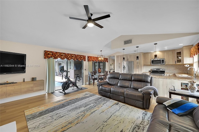 living room featuring light wood-type flooring, lofted ceiling, sink, and ceiling fan with notable chandelier