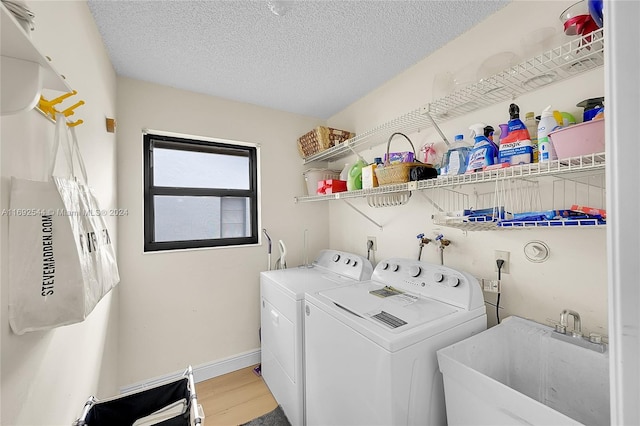 laundry area with a textured ceiling, light hardwood / wood-style floors, sink, and washing machine and clothes dryer