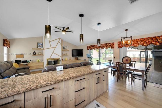 kitchen with pendant lighting, light stone countertops, lofted ceiling, ceiling fan, and light hardwood / wood-style flooring