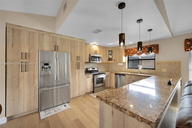 kitchen featuring stainless steel appliances, kitchen peninsula, hanging light fixtures, light hardwood / wood-style flooring, and light brown cabinetry