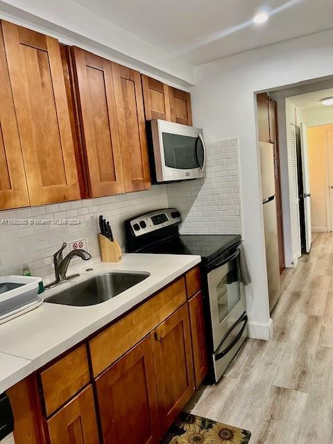 kitchen featuring decorative backsplash, sink, light wood-type flooring, and stainless steel appliances