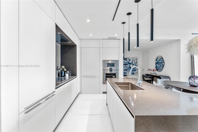 kitchen featuring stainless steel double oven, a large island, hanging light fixtures, sink, and white cabinets