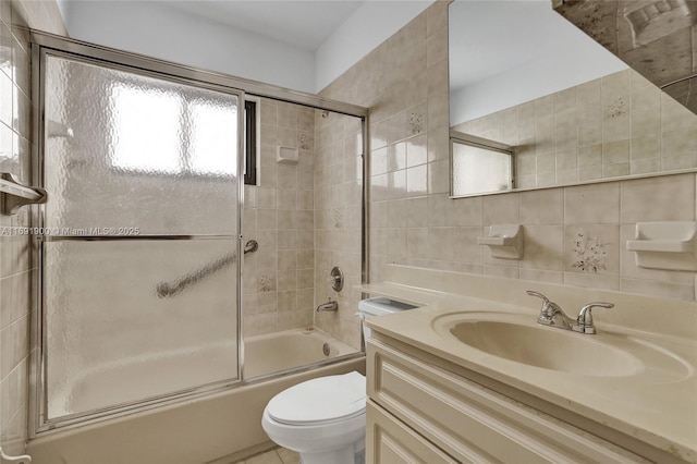 full bathroom featuring toilet, bath / shower combo with glass door, tile walls, vanity, and decorative backsplash