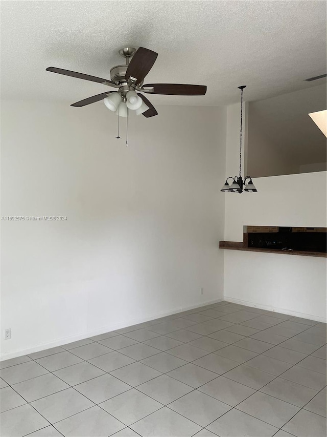 tiled empty room with ceiling fan with notable chandelier, a textured ceiling, and vaulted ceiling