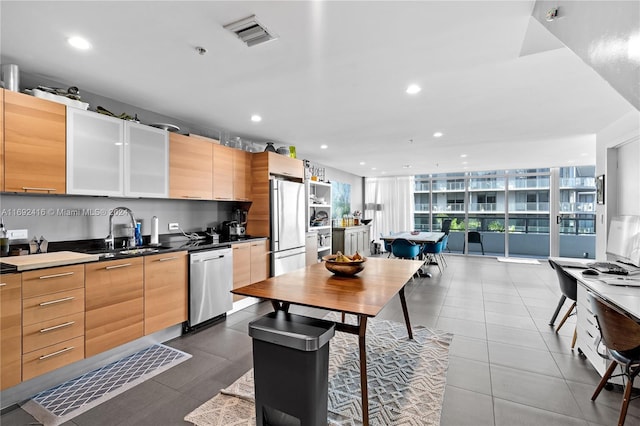 kitchen featuring stainless steel appliances, dark tile patterned floors, light brown cabinets, floor to ceiling windows, and sink