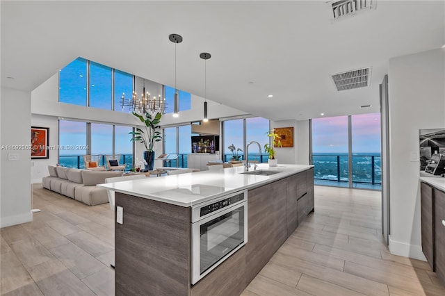 kitchen featuring light hardwood / wood-style floors, sink, a kitchen island with sink, decorative light fixtures, and stainless steel oven