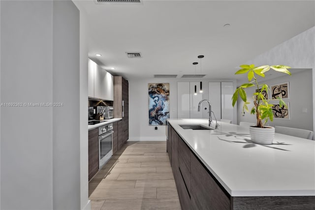 kitchen featuring light hardwood / wood-style floors, sink, dark brown cabinets, a kitchen island with sink, and stainless steel oven