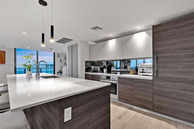 kitchen with decorative light fixtures, sink, white cabinets, oven, and a spacious island