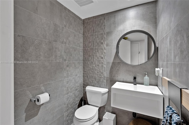 bathroom featuring toilet, tile walls, and sink