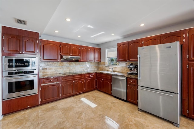 kitchen with tasteful backsplash, appliances with stainless steel finishes, sink, and light stone counters