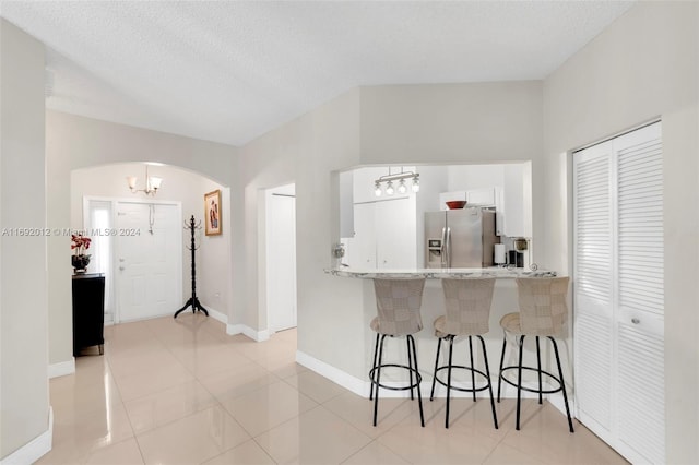 kitchen featuring a kitchen bar, stainless steel refrigerator with ice dispenser, kitchen peninsula, a textured ceiling, and white cabinetry